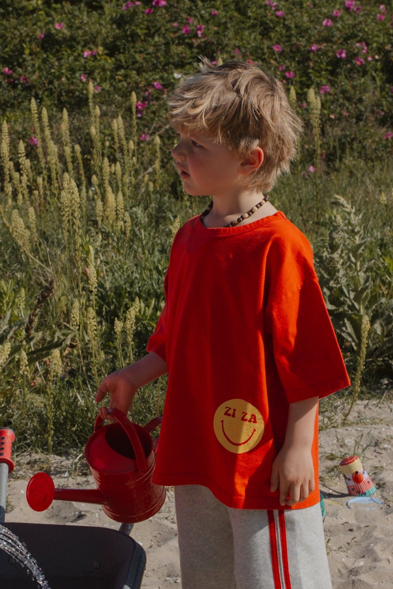 Kid wearing the red ZIZA CLUB Tee SMILE Tomato, an oversized kids t-shirt with a yellow smiley print