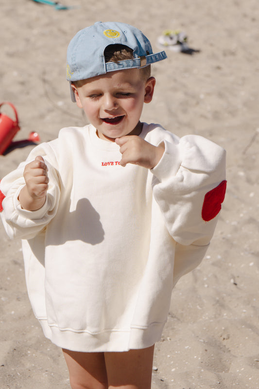 Kid wearing the ZIZA CLUB Sweater LOVE YOU Cream, an off-white oversized kids sweater with heart elbow patches