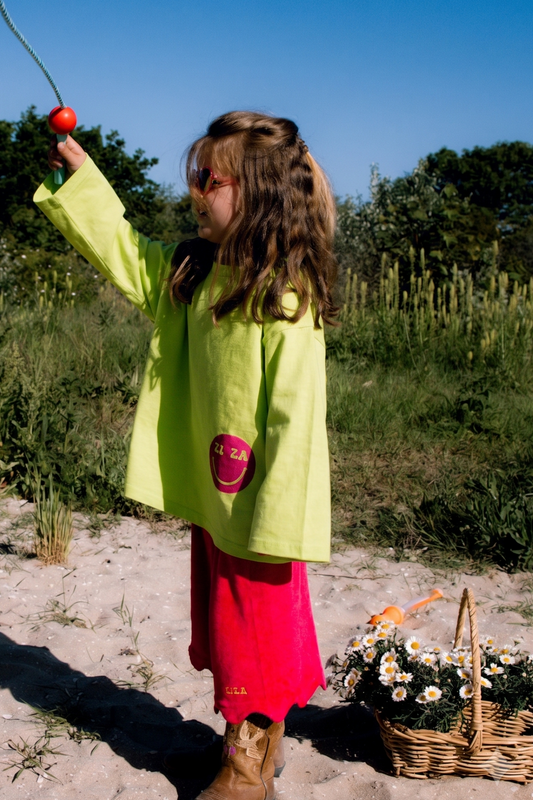 Kid wearing the ZIZA CLUB LS SMILE Apple, a green oversized kids longsleeve with a pink smiley print