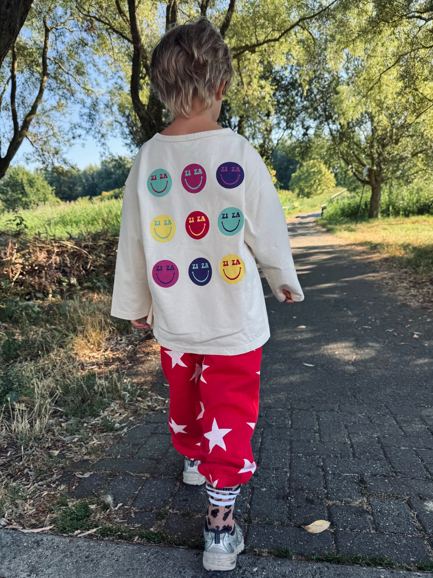 Kid wearing the ZIZA CLUB LS SMILES Cream, an off-white oversized kids longsleeve with colorful smiley prints