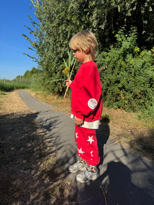 Kid wearing the ZIZA CLUB Sweater VIBES Tomato, a red oversized kids sweater with smiley elbow patches